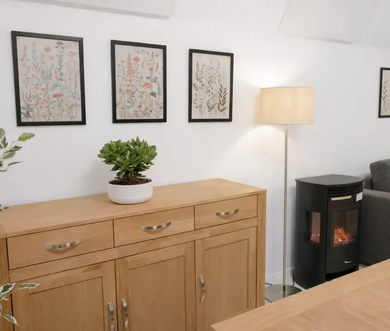 Wohnbereich im Ferienhaus Seeblick mit Sideboard, Pflanze, Bildern und Kaminofen.