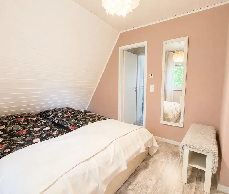 Schlafzimmer im Haus am See mit Doppelbett, Dachschraege und hellen Einbauschraenken.
