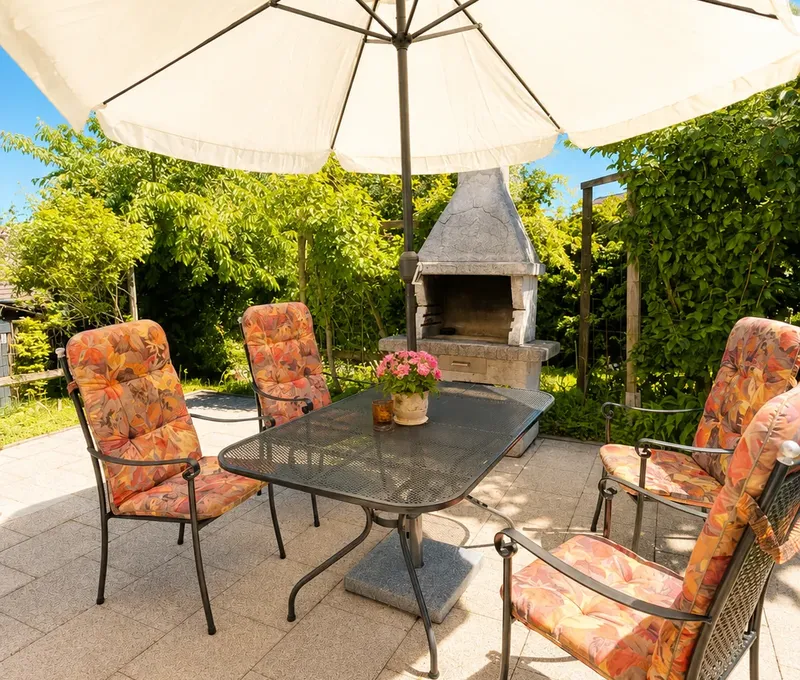 Terrasse am Haus am See mit Sonnenschirm, Sitzgruppe und Blick ins Gruene.