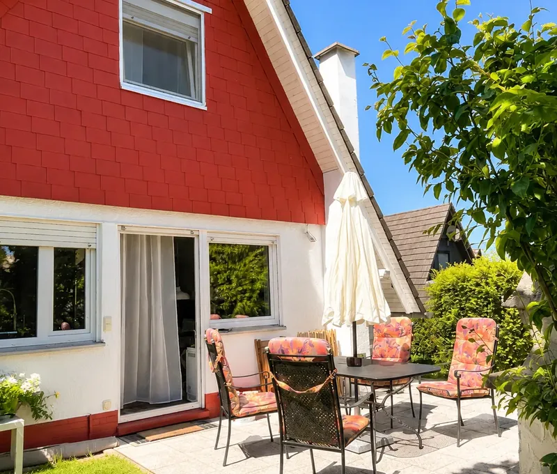 Aussenansicht vom Haus am See mit roter Fassade, Terrasse und Garten.
