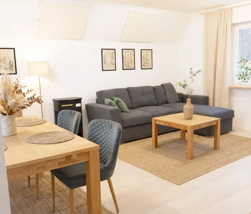 Wohnzimmer im Ferienhaus Seeblick mit Sofa, Couchtisch, Bildern und hellem Fenster.