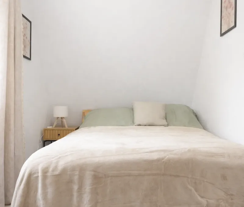 Schlafzimmer im Ferienhaus Seeblick mit Bett, Nachttisch und hellen Vorh&auml;ngen.