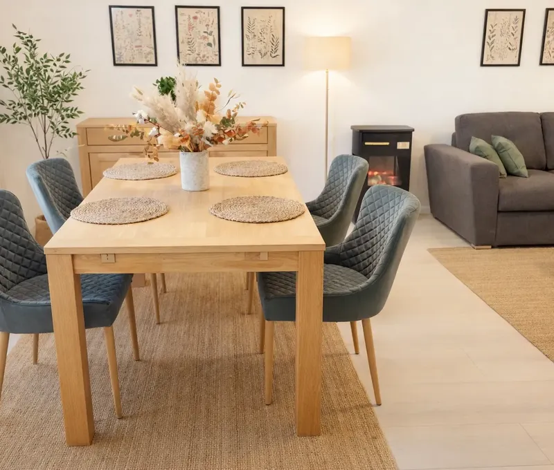 Essbereich im Ferienhaus Seeblick mit Holztisch, gepolsterten St&uuml;hlen und Sofa im Hintergrund.