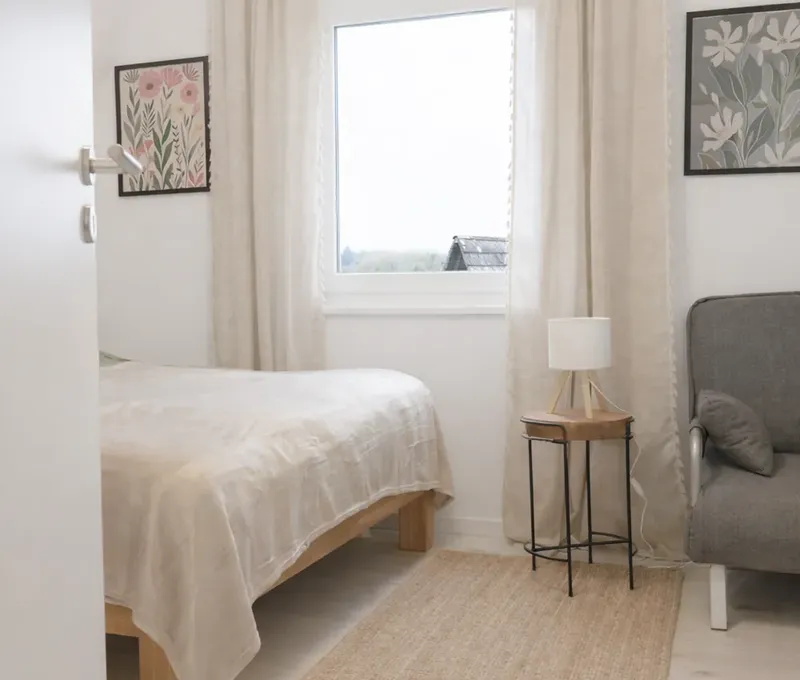 Helles Schlafzimmer im Ferienhaus Seeblick mit Doppelbett, Fenster und kleinem Stuhl.