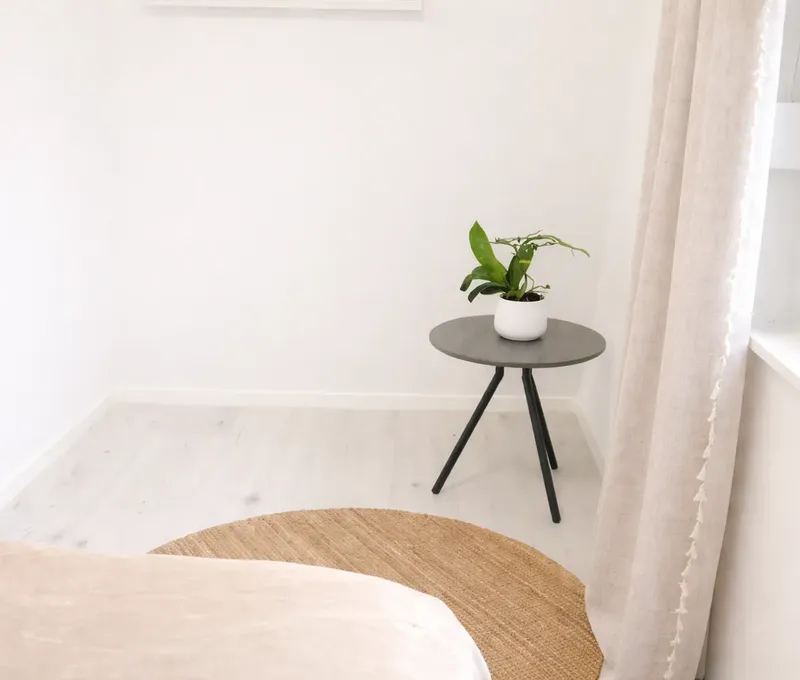 Schlafzimmerdetail im Ferienhaus Seeblick mit Bett, Beistelltisch, Pflanze und Fenster.